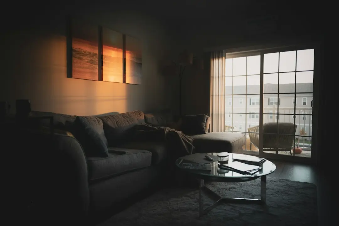 A dim living room with a gray sectional sofa and a round glass coffee table, a quiet place to subscribe to XerquvaTV IPTV